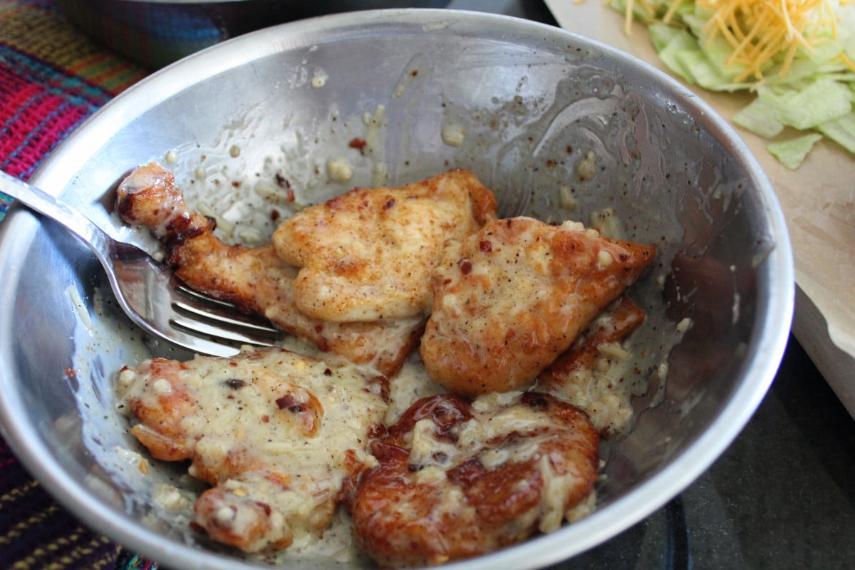 overhead shot of garlic parmesan wing sauce on fried chicken in a bowl.
