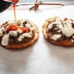 side shot of buffalo sauce being drizzled over ground beef and beans tostadas