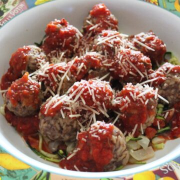 large serving dish with porcupine meatballs and zoodles with spaghetti sauce on top.