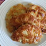 saltine cracker coated fried pork chops stacked on each other on a plate with a cloth napkin next to it.