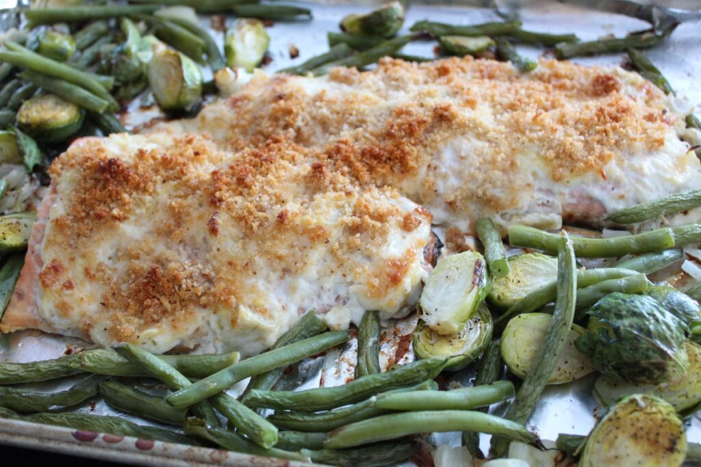 coated breadcrumb baked salmon on a baking sheet with green beans and brussels sprouts on a baking sheet.