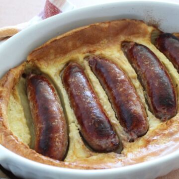 baking dish with bratwursts baked in a savory pudding with a cloth napkin next to it.