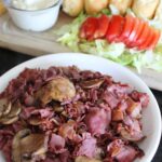long shot of a sandwich board with cooked beef and sandwich toppings.