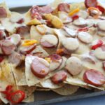 side shot of nachos with cheese sauce and sausage.