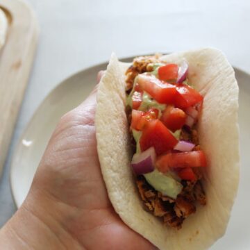 a hand holding a salmon taco in it with more taco ingredients and a plate underneath.