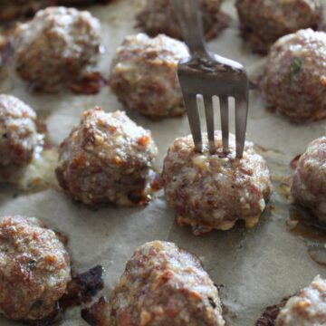 meatballs on a baking sheet with a fork stuck into one meatball.