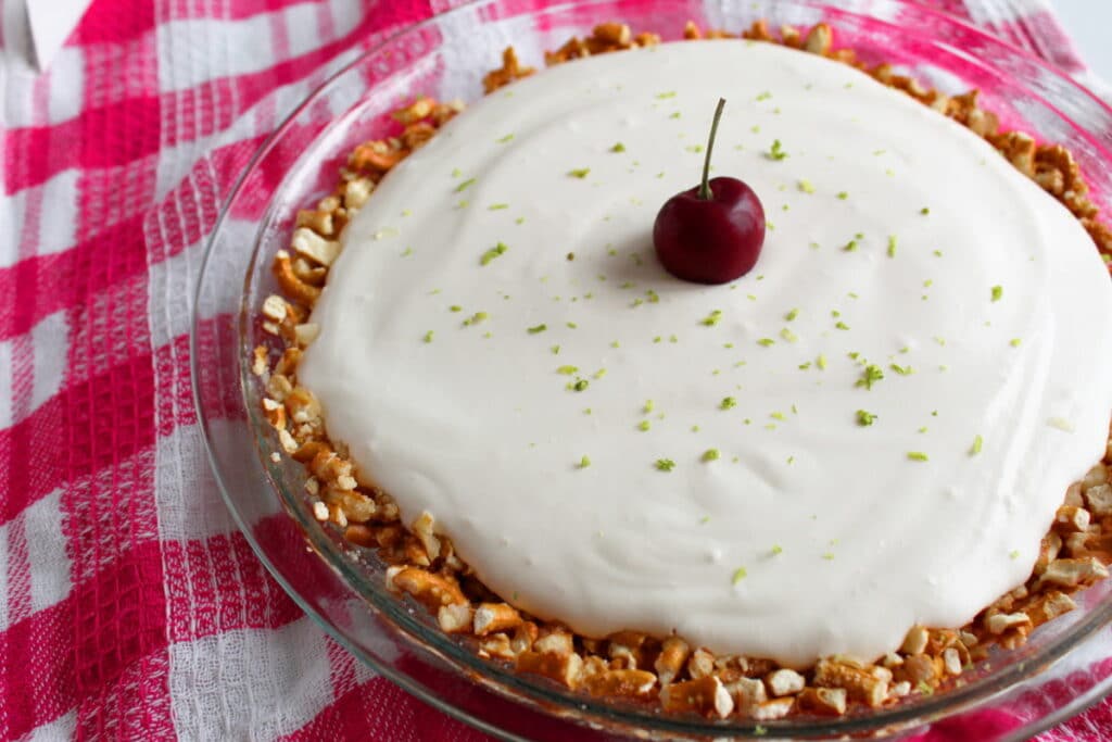 cherry limeade pretzel pie in a pie pan with lime and a cherry on top