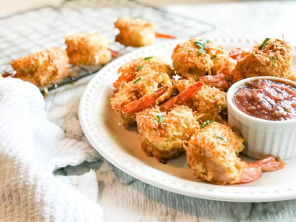 coconut shrimp on a plate with shrimp on a skewer and dipping sauce