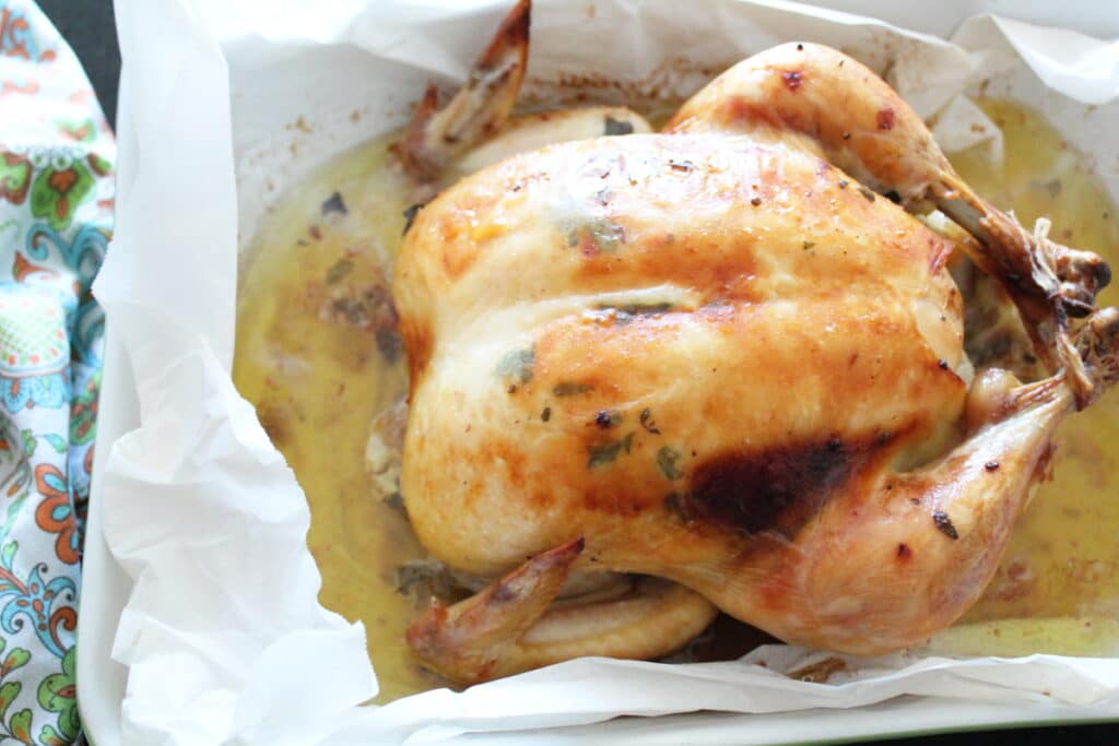 shot of a whole baked chicken in parchment paper in a baking dish with a cloth napkin next to it.