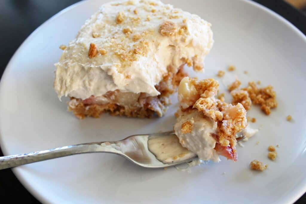 zoomed in shot of a slice of chunky applesauce cheesecake with a bite out of it and a fork on the plate