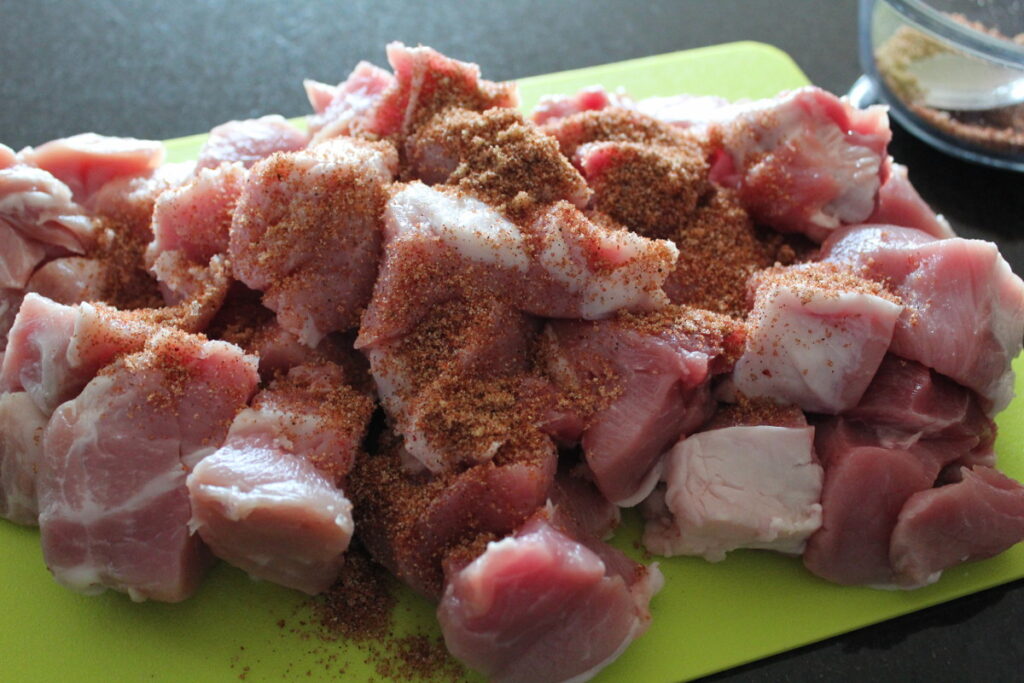 cubed pork on a cutting board covered with dry rub.