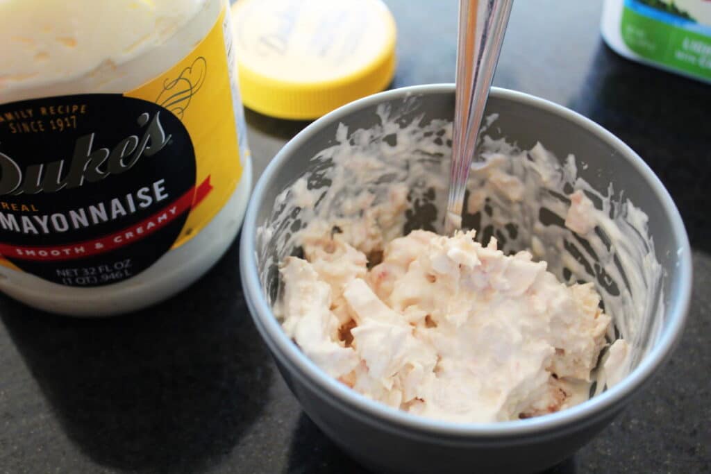 a bowl with creamy tuna salad in it with a spoon and a jar of mayonnaise next to it with the cap off