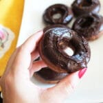 zoomed in shot of a hand holding a death by dark chocolate donut with a platter of more donuts and a towel next to it in the background.