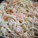 a side shot of a pan of prepared shrimp spaghetti with a creamy mayo based sauce.