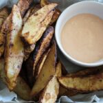 overhead shot of air fryer potato wedges with a side of dipping sauce in a bowl next to them.