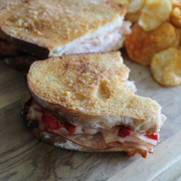 side shot of a turkey sandwich cut in half on a cutting board. a pile of bbq potato chips on the side.
