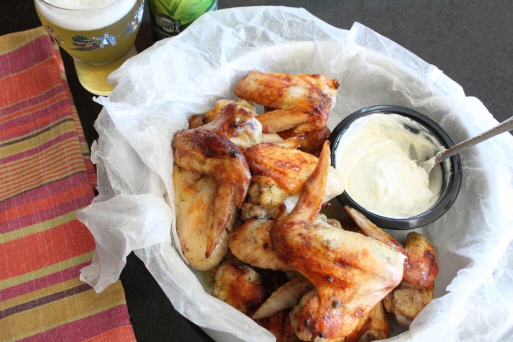 overhead shot of baked chicken wings with dipping sauce and a cold beer next to it.
