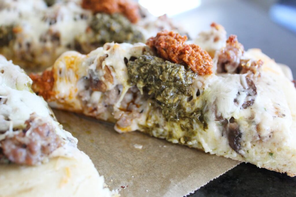 side shot of a slice of pizza with sausage and pesto.