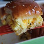 side shot of a spatula holding up a scrambled egg hawaiian roll sandwich.