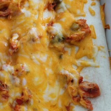 chicken burritos in a baking dish topped with cheese and salsal.