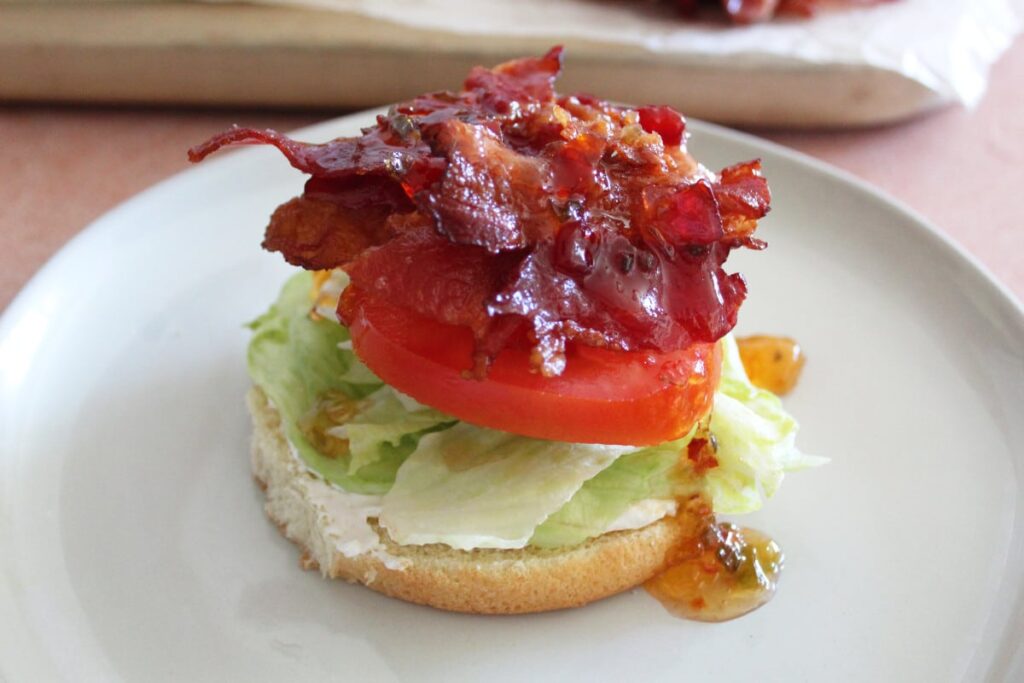 a bun topped with lettuce tomato bacon and pepper jelly on a plate.