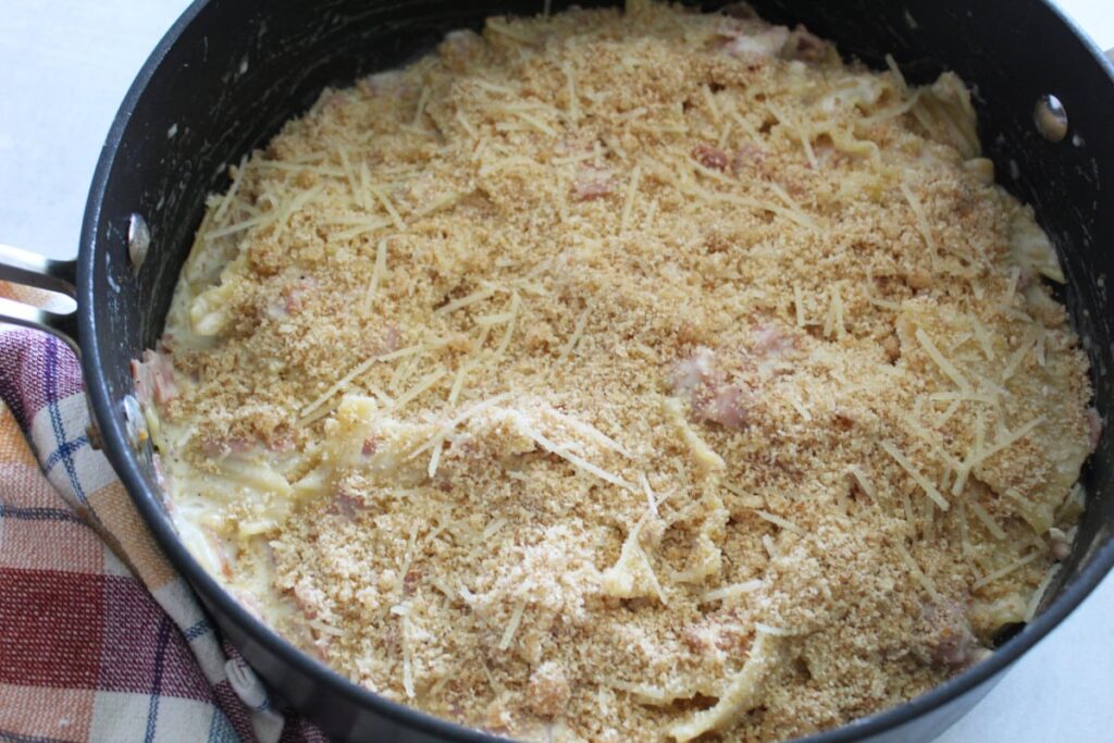 skillet holding pasta with sauce and bread crumbs covering the top. a cloth napkin next to the pan.